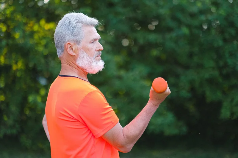 Older man performing a dumbbell curl outdoors